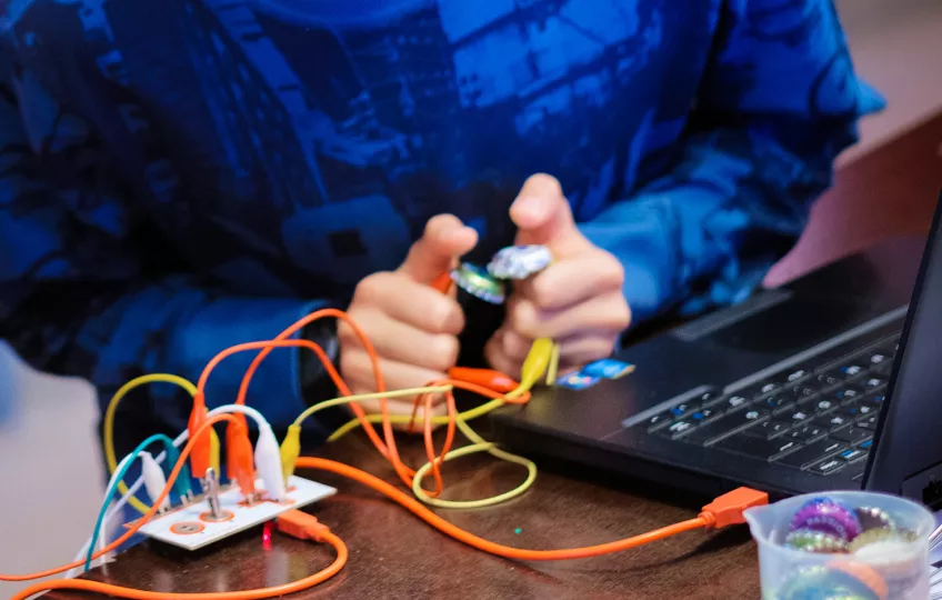 A child is doing a science experiment with a laptop and cords. Photo.