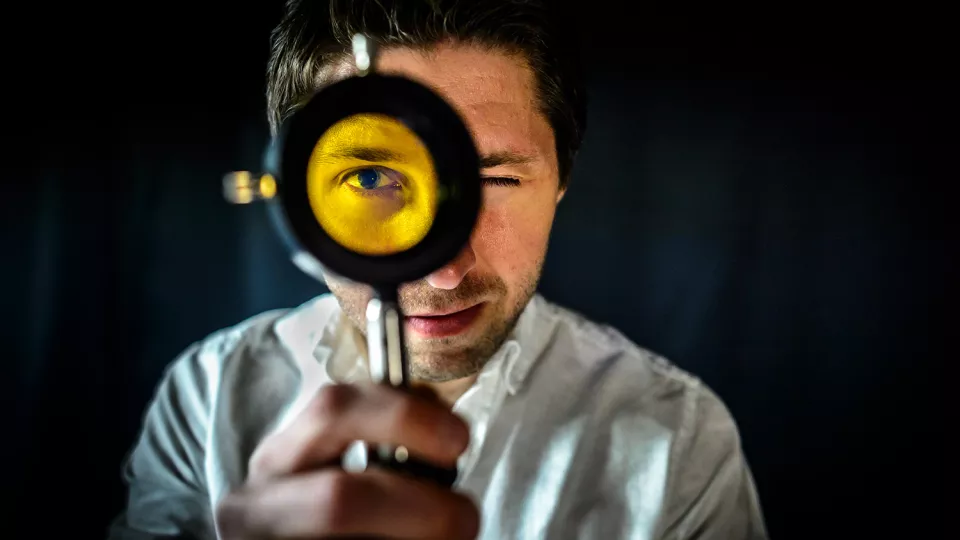 A man with a magnifying glass in front of his eye. Photo.