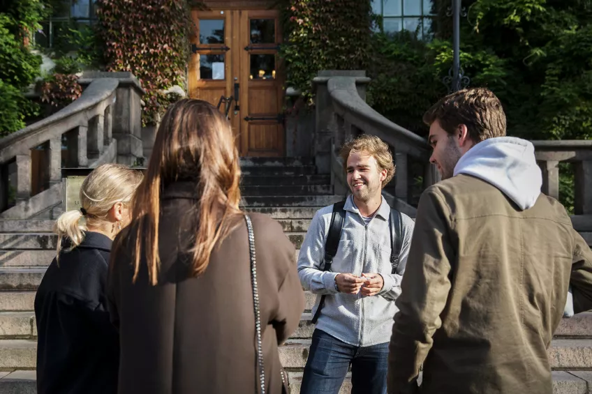 A group of students talking in front of a building. Photo.