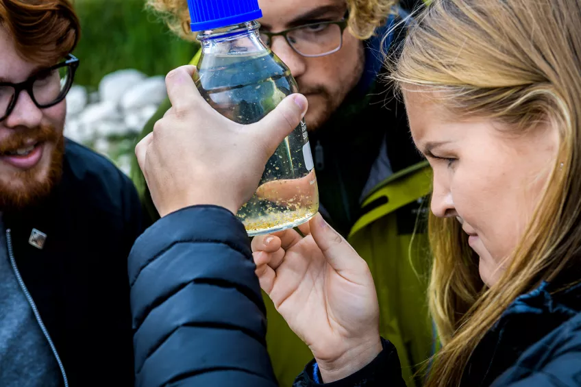 Three students looking at a water sample in a bottle. Photo: Kennet Ruona.