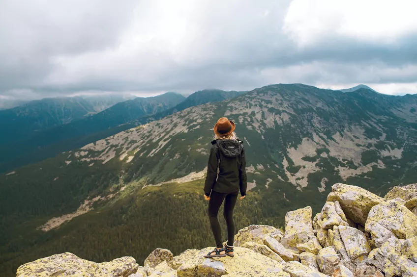 Woman standing on a mountain, looking out over the landscape. Photo.